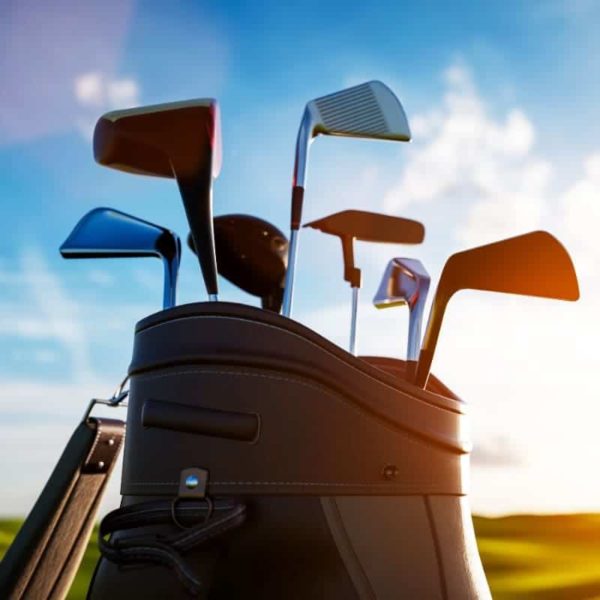 A close-up of a golf bag filled with various golf clubs stands against a clear blue sky with a bright sun, symbolizing the perfect day for teeing off and making payments on the greens.