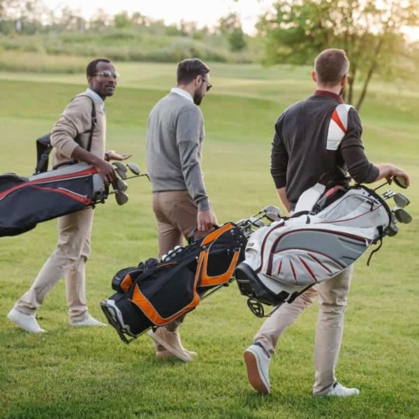 Three men walking on a golf course, each carrying a golf bag, discuss the latest innovations in payment processing.