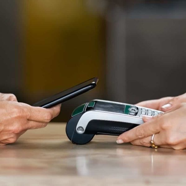 A person seamlessly settles their invoice by using the Pay Your Invoice feature to make a contactless payment with their smartphone at a card reader terminal on a wooden table.