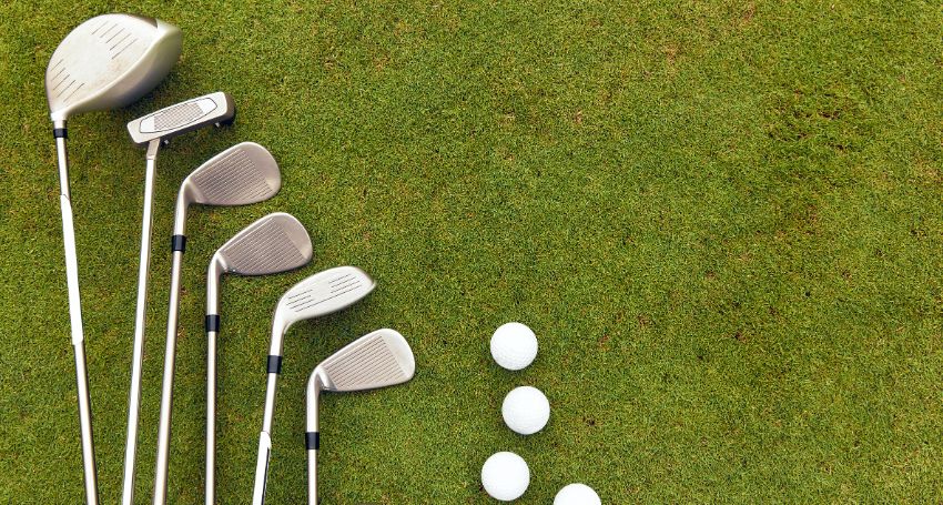 Six golf clubs of various golf club types and six golf balls arranged on grass, with the clubs aligned on the left and balls positioned in two columns on the right.