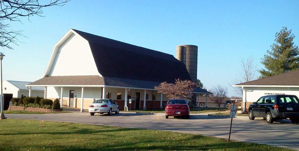 A barn-style building with a silo stands next to a parking lot in Centerville, VA, where two cars are parked, capturing the serene backdrop of a nearby golf club.