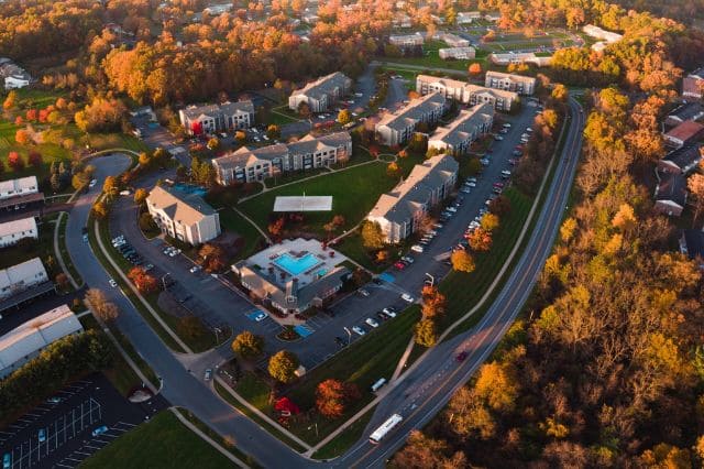 Aerial view of a residential complex with multiple buildings, parking areas, and surrounded by autumn trees. Roads encircle the property, offering easy access to nearby amenities like SwingFit for top-notch golf club fitting and practice sessions.