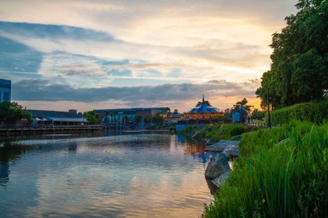 A serene pond at sunset with a lush green shoreline, distant structures, and a partly cloudy sky reflecting on the water, creating the perfect backdrop for a relaxing SwingFit session.