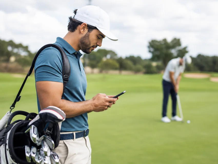 Golfer checking a phone beside a golf bag on the course