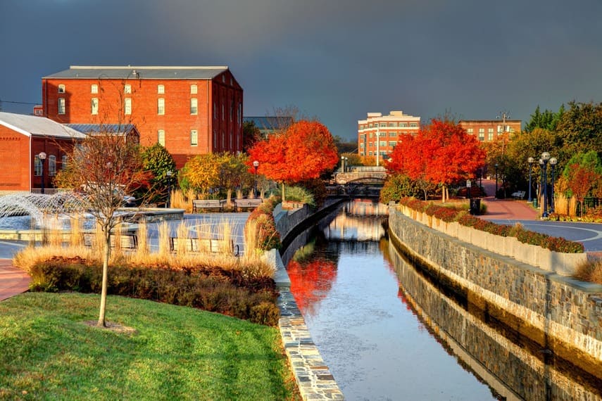 A canal lined with stone walls and autumn trees runs between red-brick buildings under a dark, cloudy sky.