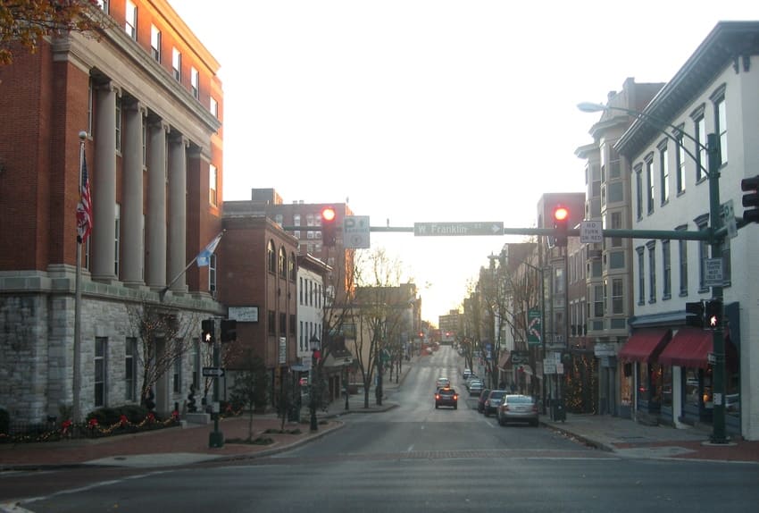 A view of a quiet city street intersection with red traffic lights, lined with historic buildings and parked cars on both sides.