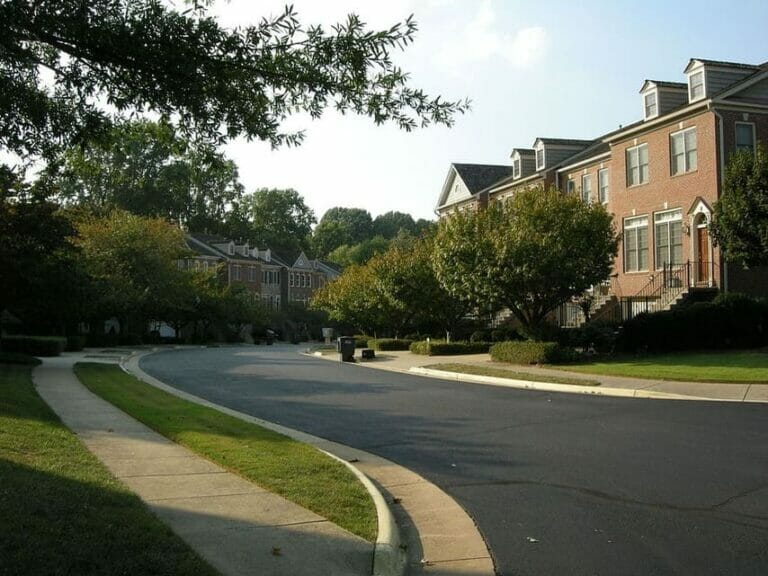A quiet suburban street lined with trees and brick townhouses on a sunny day.